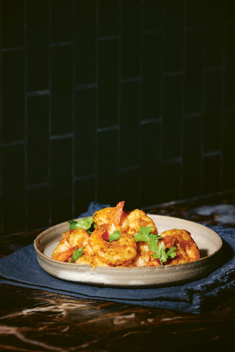 prawns seasoned with gunpowder garam masala, garnished with cilantro in a white bowl on a brown stone table top