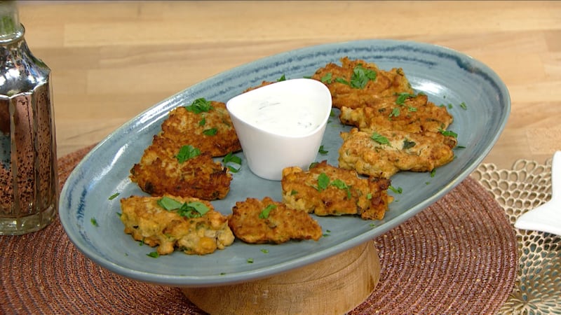 Eight light brown and lightly fried oval-shaped chickpea patties with green parsley garnish (chopped) plated on a blue-grey oval plate with white garlic sauce in the middle