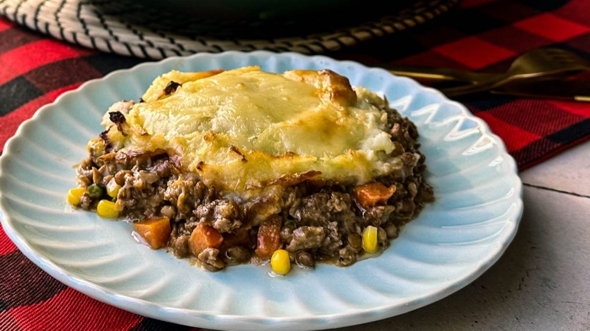 Slice of Shepherd's Pie on a light blue scalloped plate, showing layers of meat and vegetables topped with golden brown mashed potatoes.