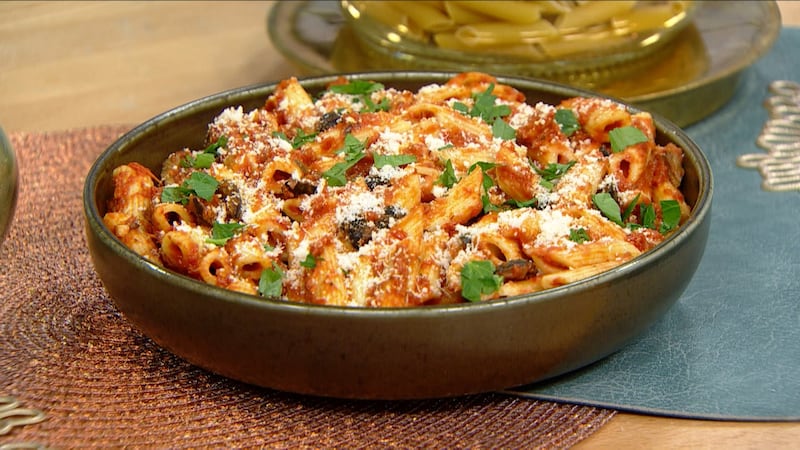 Penne pasta covered in red tomato sauce and white parmesan cheese with bits of black olives and green parsley