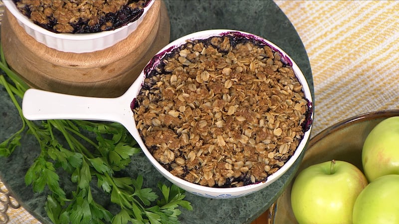 Roasted and light brown rolled oats mixed with brown sugar atop a dark purple blueberry mix, in a white casserole dish.