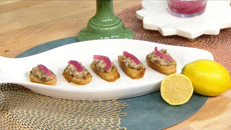 Five slices of light brown, toasted and oiled sourdough baguette topped with sardine salad (sardines mixed with mayo) and a slice of pink pickled shallot on top
